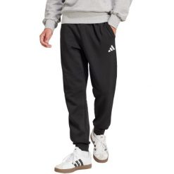 Spodnie męskie adidas Essentials Feelcozy. Czarne spodnie materiałowe męskie Adidas, bez wzorów, z bawełny, z standardowym stanem. Za 171.99 zł.