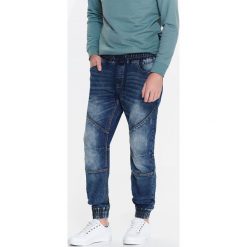 SPODNIE MĘSKIE TYPU JOGGER Z DZIANINY IMITUJĄCEJ JEANS. Niebieskie spodnie materiałowe męskie TOP SECRET, bez wzorów, z jeansu. W wyprzedaży za 64.99 zł.