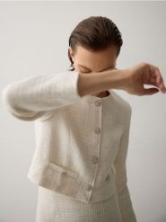 Krótki żakiet z tkaniny boucle - złamana biel. Marynarki i żakiety damskie Reserved, bez wzorów, z bawełny, bez kołnierzyka, bez ramiączek. W wyprzedaży za 119.99 zł.